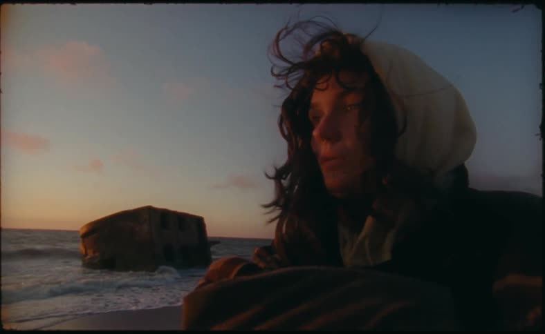 A woman is standing outdoors at the beach during sunset