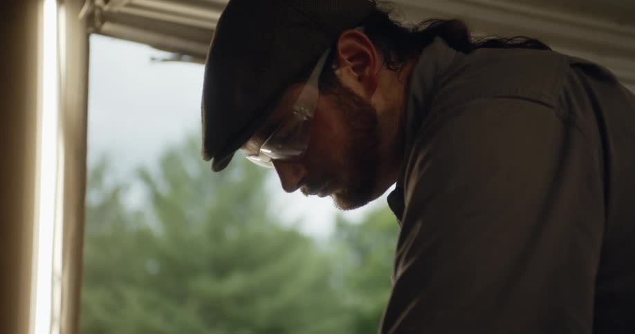 A man stands with his head down next to an open window