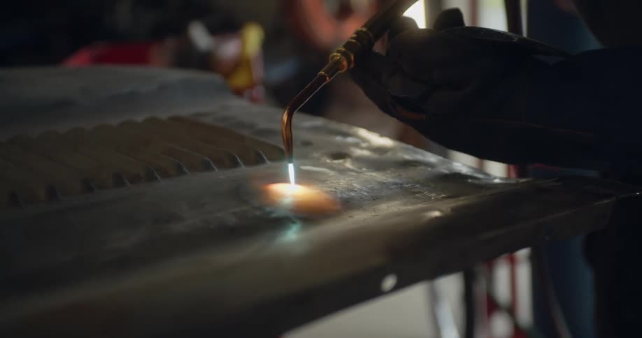 A person in a workshop uses a torch to heat a metal sheet