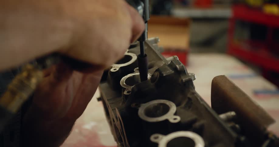 A man uses a drill on a piece of machinery in his garage