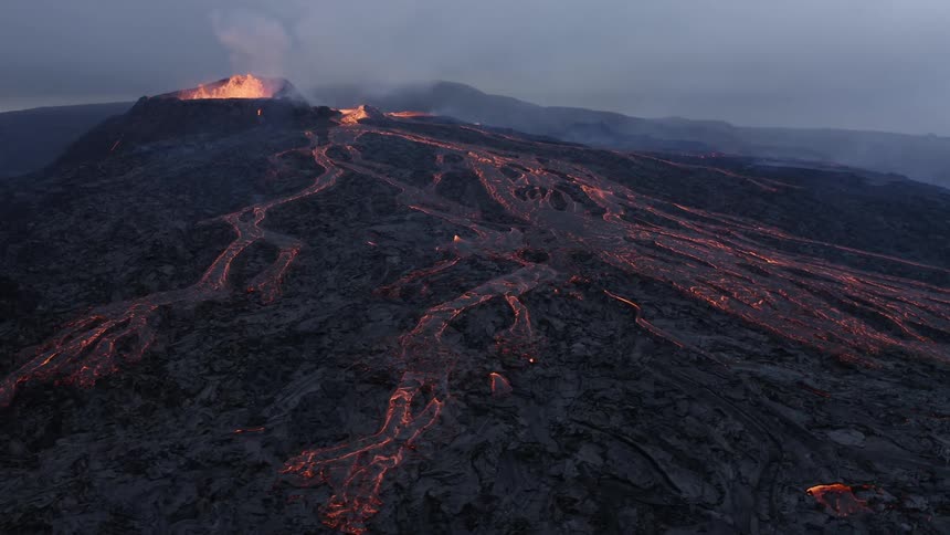 Hot lava flows down the sides of a volcanic mountain and molten lava splashes as it erupts