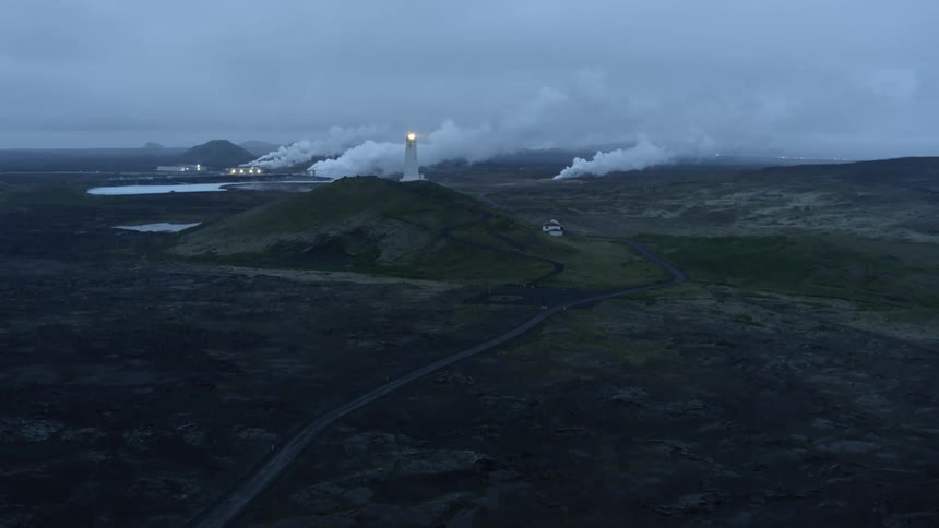 A lighthouse is on top of a mountain near water and factories