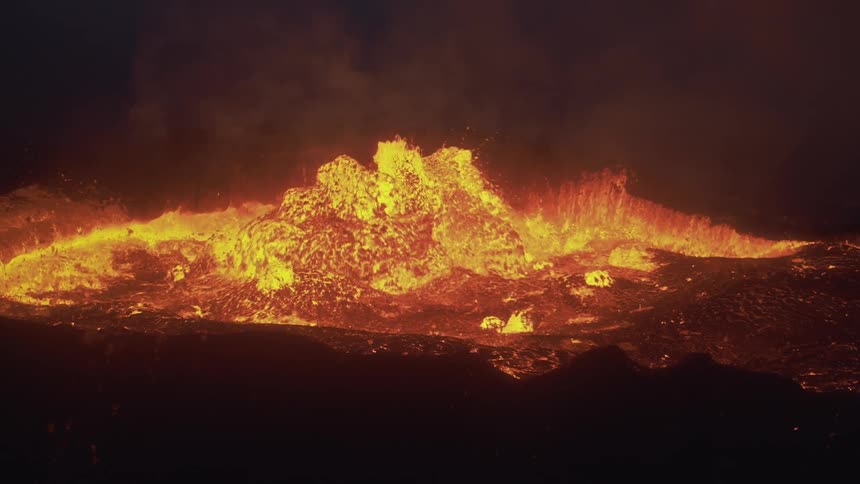 Smoke rises and hot lava splashes as a volcano erupts in the darkness