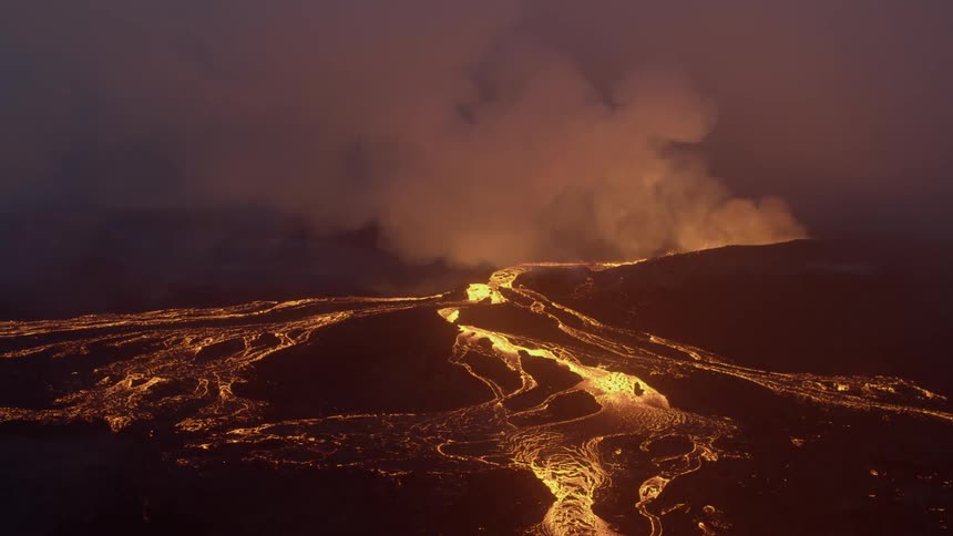A volcano erupts and spills lava onto the ground below