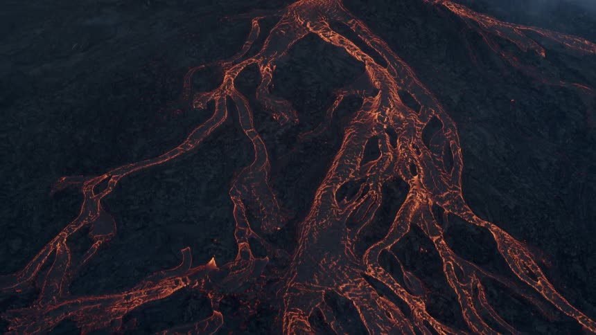 Hot lava glows as it rapidly flows down the sides of an erupting volcanic mountain