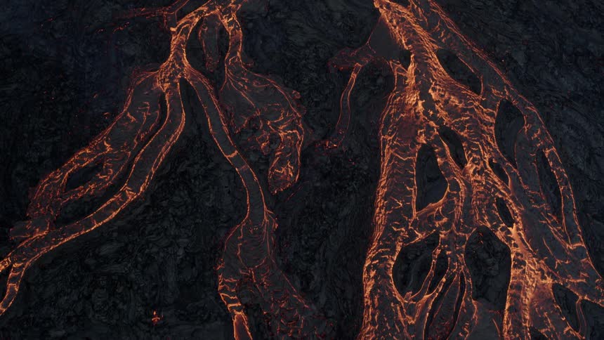 Streams of lava flow down side of volcano the orange glowing through the dark ash