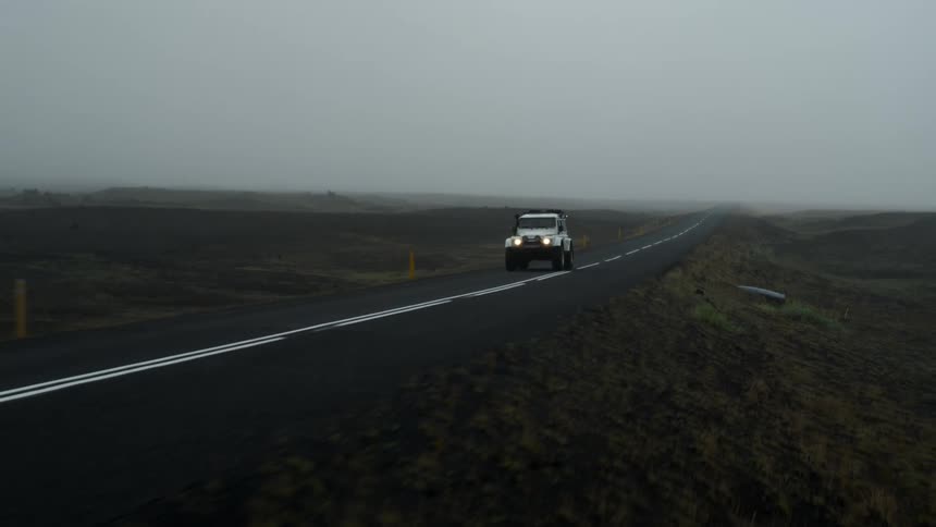 An automobile is traveling on a foggy rural road and there are mountains on the horizon