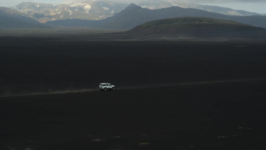 A sport utility vehicle drives down a rural road near a mountain range