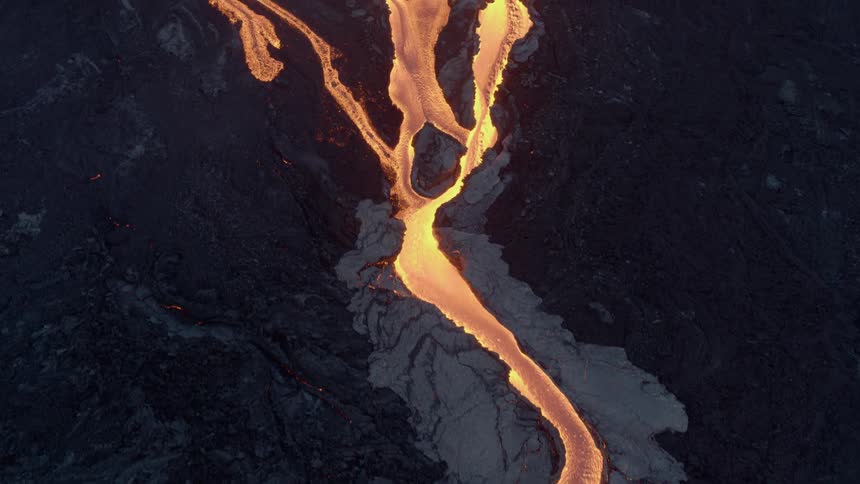 A river of glowing hot lava flows in the darkness from an erupting volcano