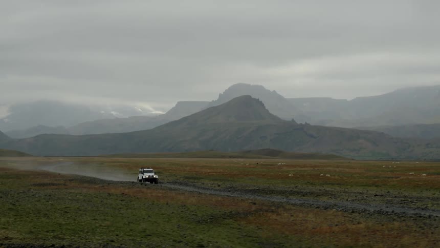 A sport utility vehicle leaves a misty trail while driving down a rural road through a field