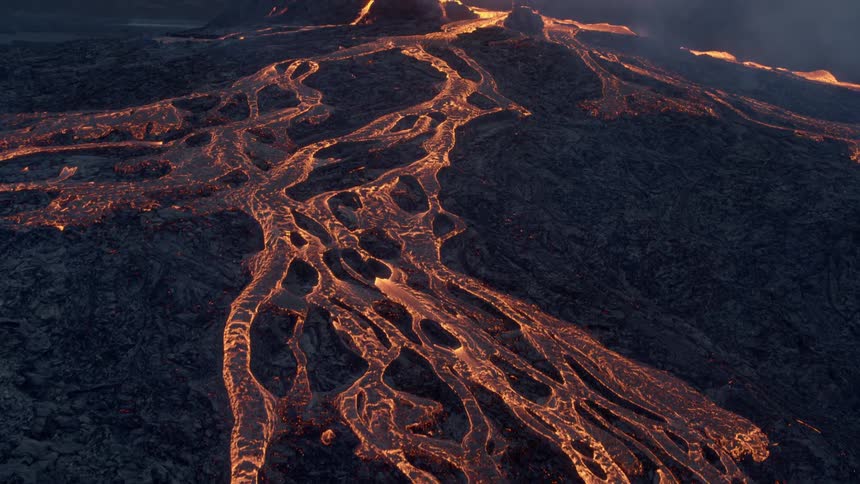 Lava bursts and splashes in volcano crater then flows orange and ashy down black of slope