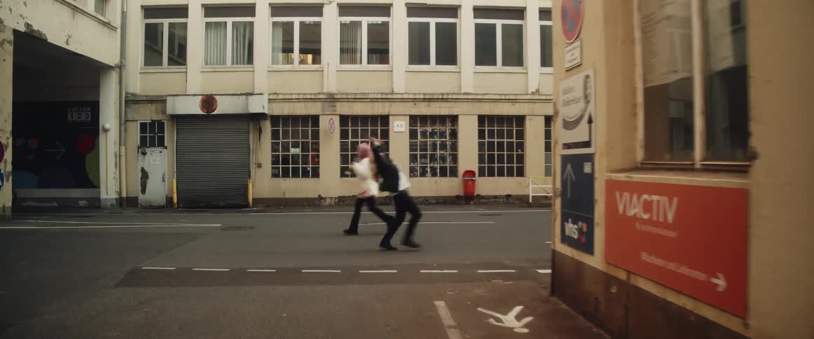 Two women laugh as they run down the middle of a city street