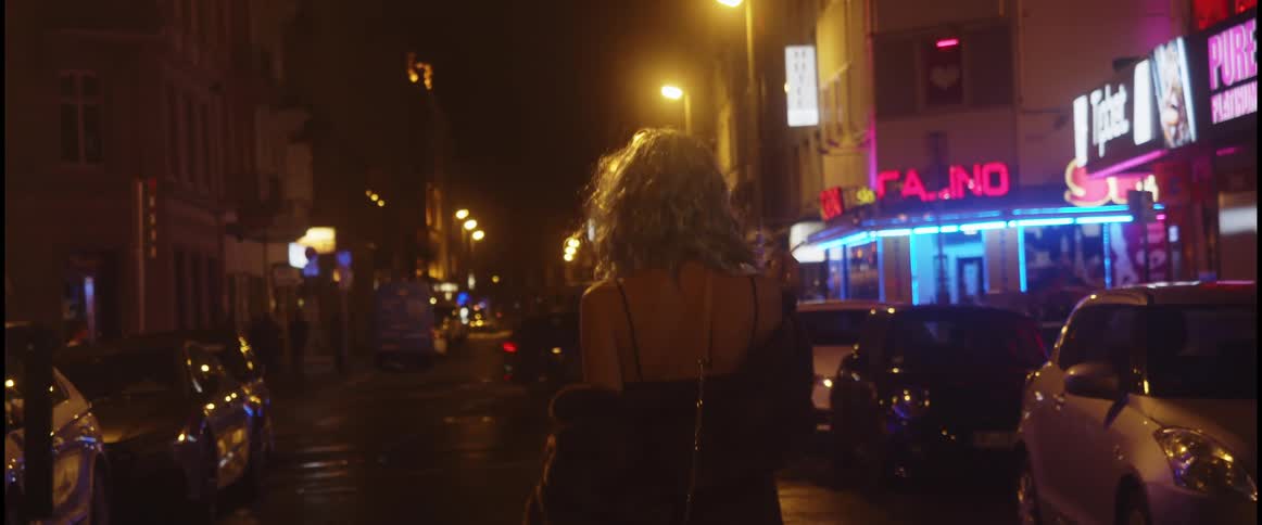 Young woman wearing a dress walks on the middle of the city street at night