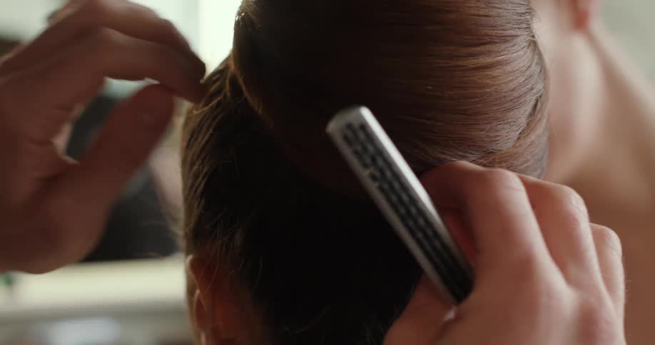 A woman sits and has her hair styled as someone else puts on her make up