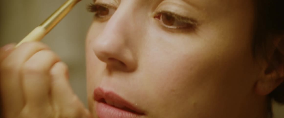 A woman applies makeup to various parts of her face using a makeup brush