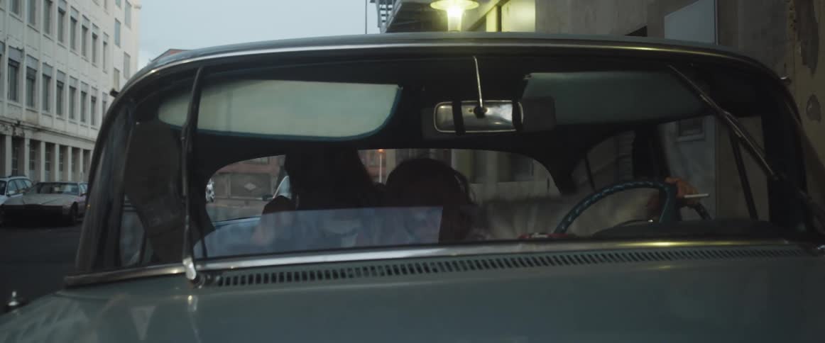 Two people are sitting in a car in a downtown city