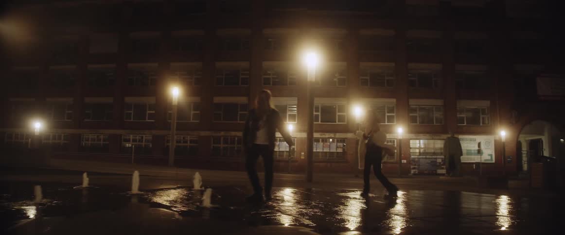 Young couple playfuly walking over a fountain on the city streets at night