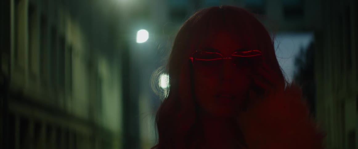 A woman wearing sunglasses is standing outside on a city street at night