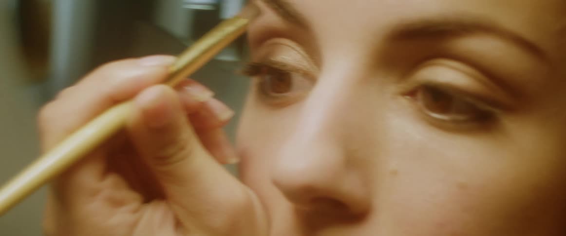 A woman is putting makeup on her eyebrow with a makeup brush