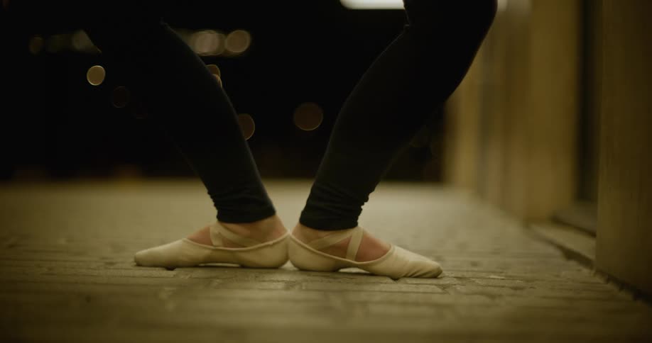 A ballet dancer leaps into the air on a brick walkway