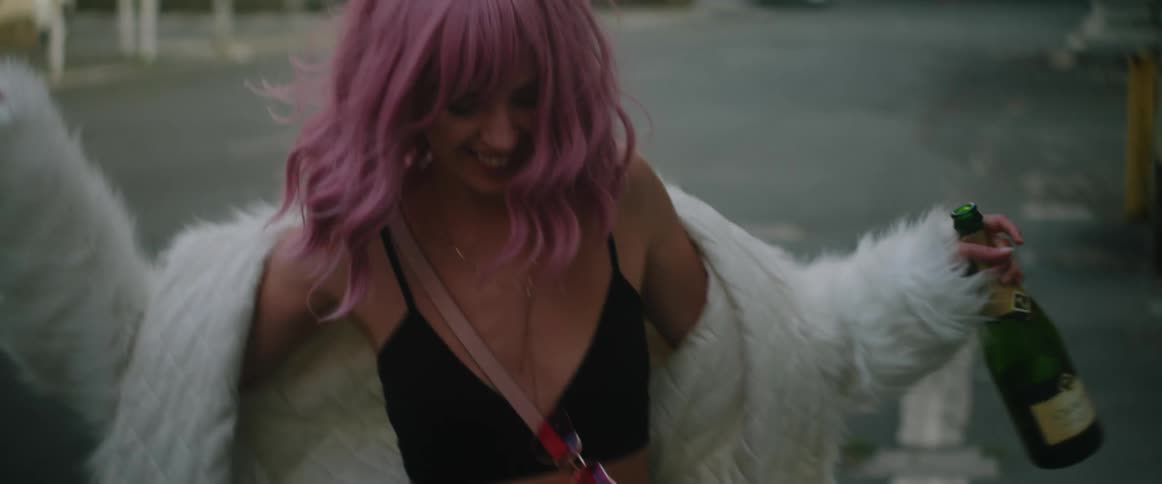A woman with pink hair is smiling as she walks on a street wearing a white fur coat and carrying a wine bottle