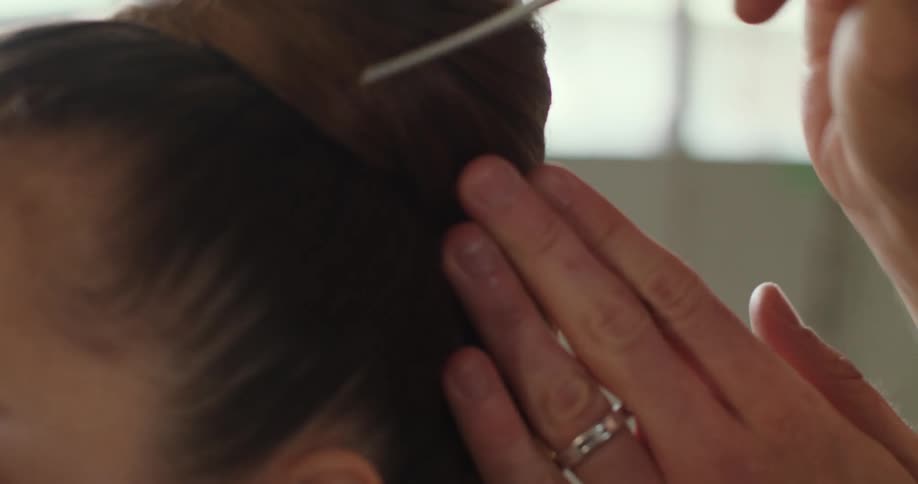 A woman is having her hair carefully styled into a bun by another person