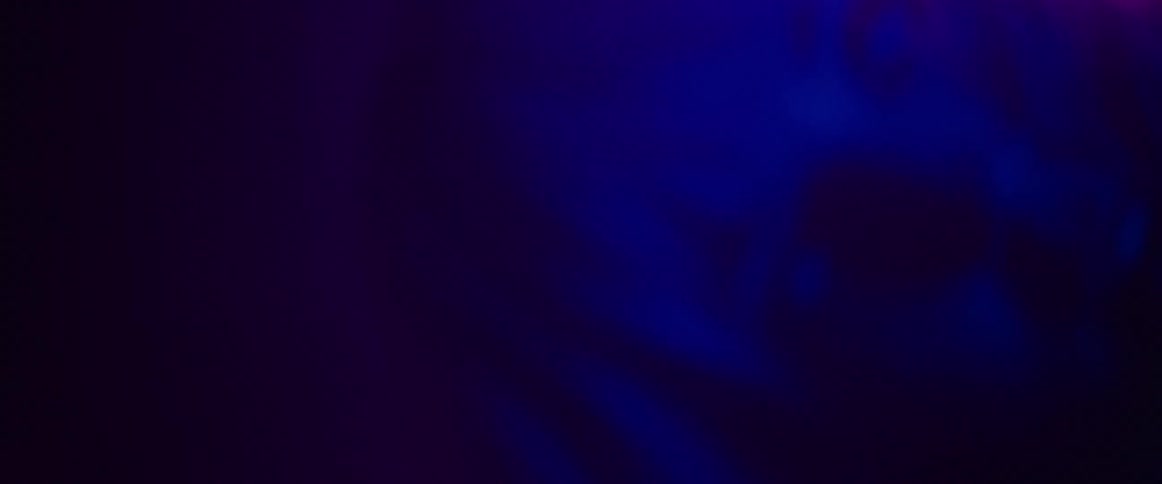 A pink light is shining on a blond woman as she smiles and moves her head