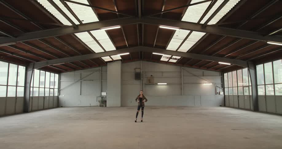 A woman stands with her hands on her hips in an empty hangar