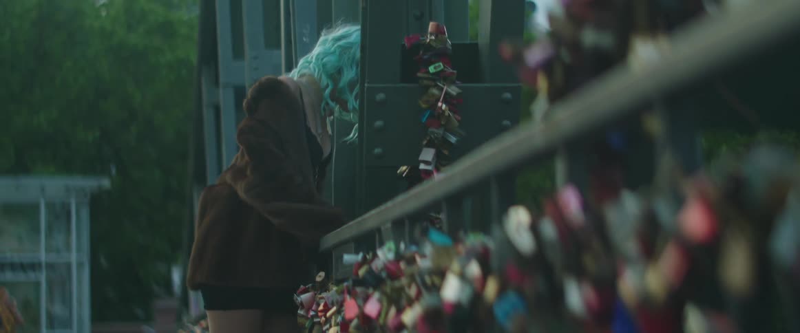 A woman leans against a bridge filled with colorful locks
