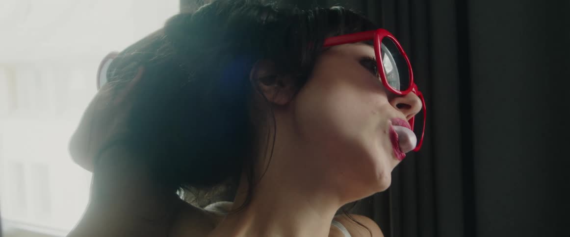 A woman blows a bubble with chewing gum while leaning against a mirror