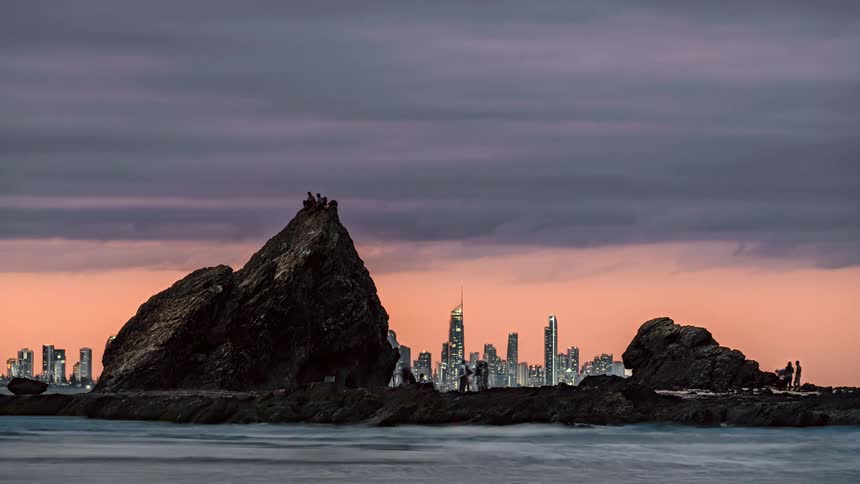 A group of people hang out on rocks along the coast with views of downtown