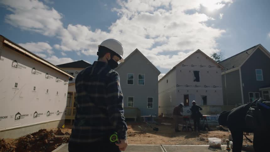 A construction worker is walking to a housing development they are building and the crew is outside working