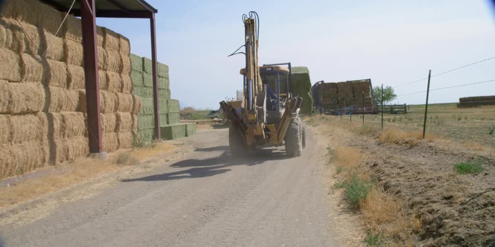 A piece of farming equipment travelling past stacked hay bales