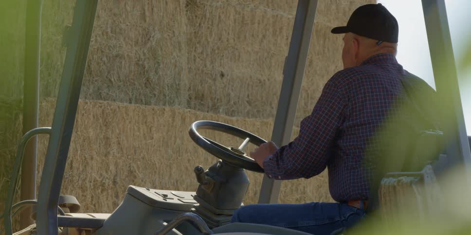 A farmer backs a tractor away from bales of hay