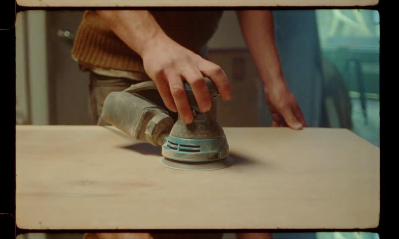 A carpenter sands the top of a wooden table