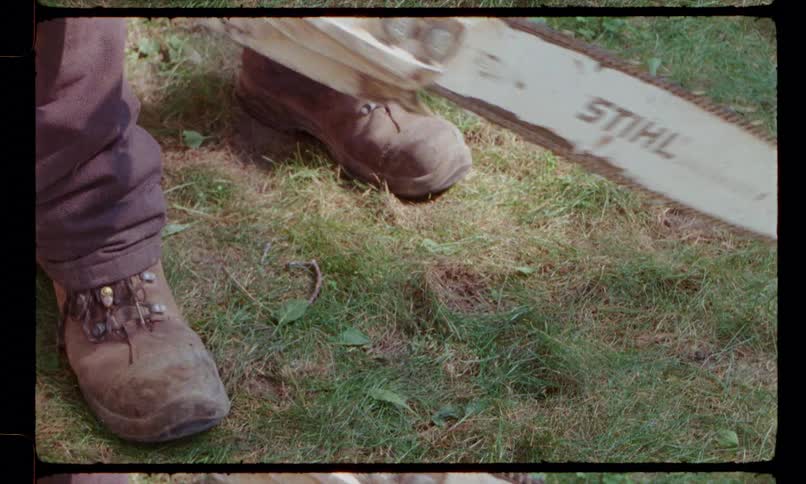 A man is standing over a chainsaw sitting on the ground and he uses one hand to hold it steady and pulls the cord to start it