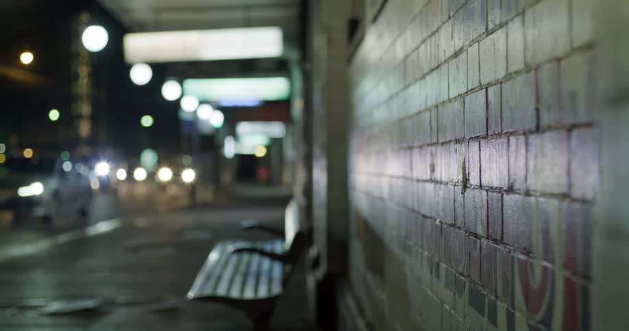 Traffic on busy street at night passes by empty bench