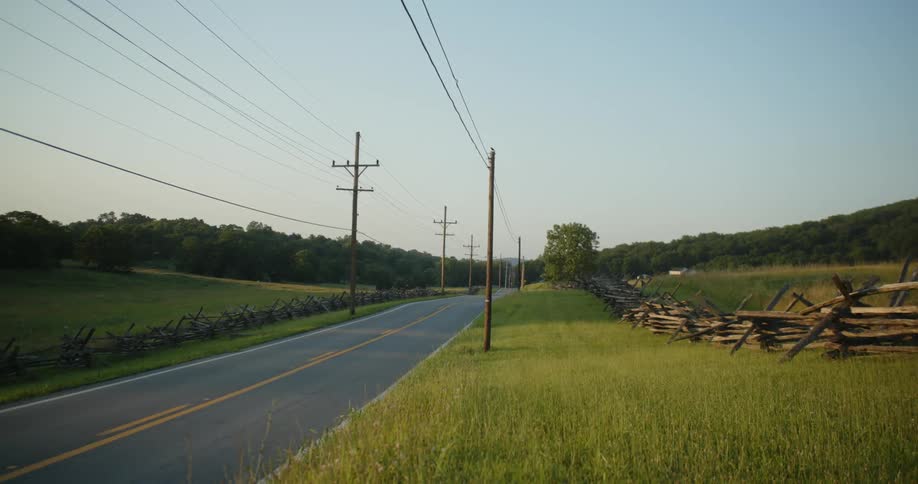 A person drives a motorcycle on a street in a rural area past grassy fields