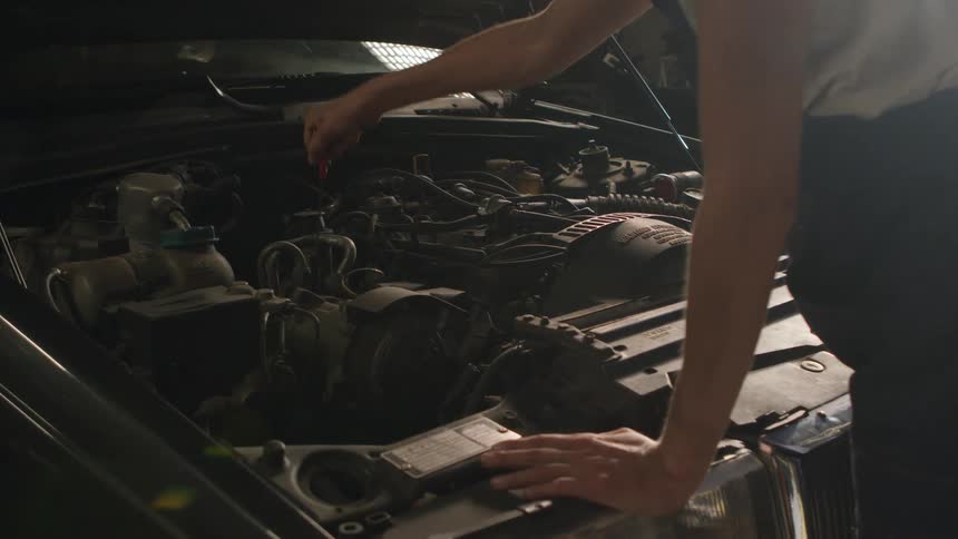 A person leans over the hood of a car and takes the oil stick out