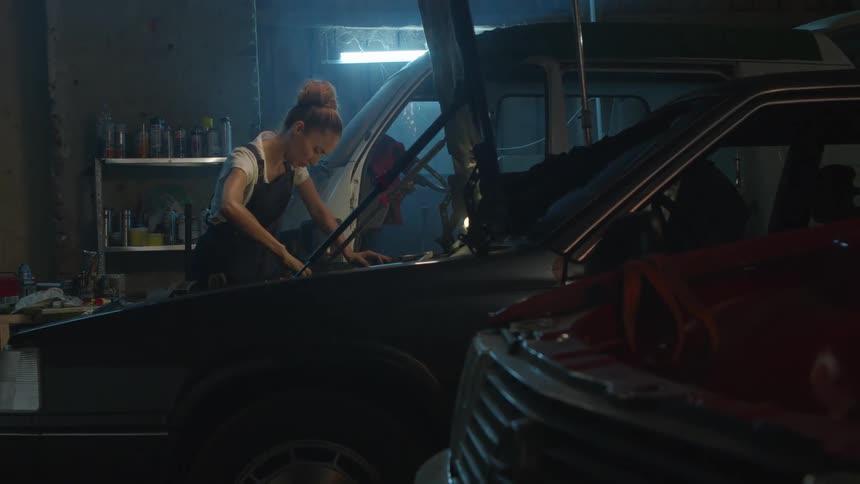 A young woman is working on a car and trying to fix it