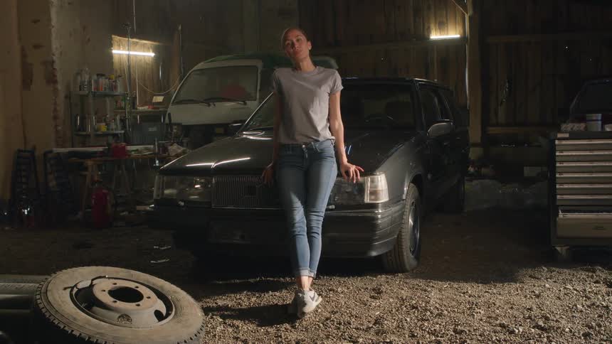 A woman leans against and poses on the hood of a car