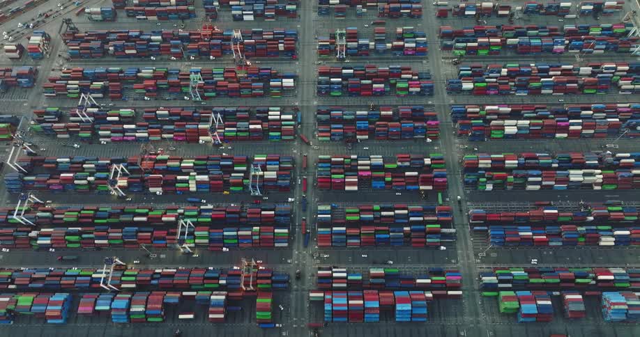 Shipping containers are neatly stacked as trucks move around the shipping yard