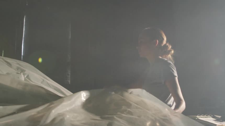 A woman uncovers a car covered with plastic