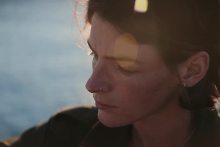 A sad looking woman outside turns her head and looks around