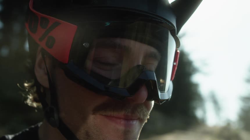 A man with a helmet and goggles on smiles outside