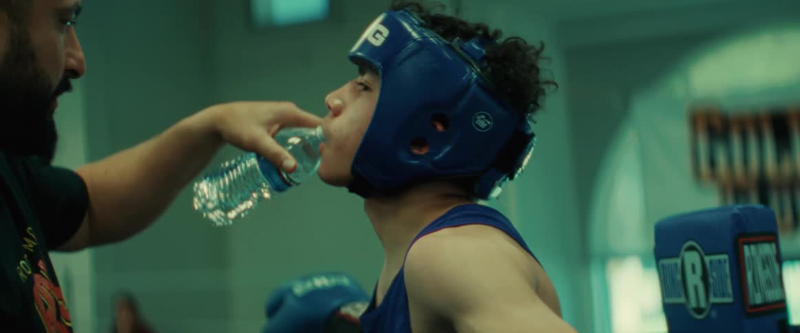 A trainer gives a hispanic boxer in the ring a drink of water