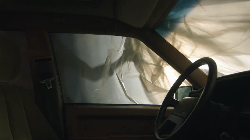 View from inside an automobile parked in a garage as someone pulls away the cloth cover