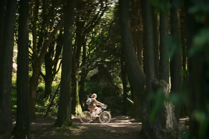 Female cyclist pedals slowly along track through woods on windy day