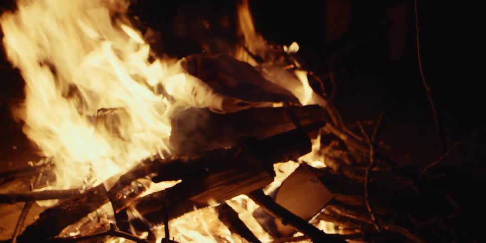Bright fire and flames glow in the darkness as the wood from a campfire burns