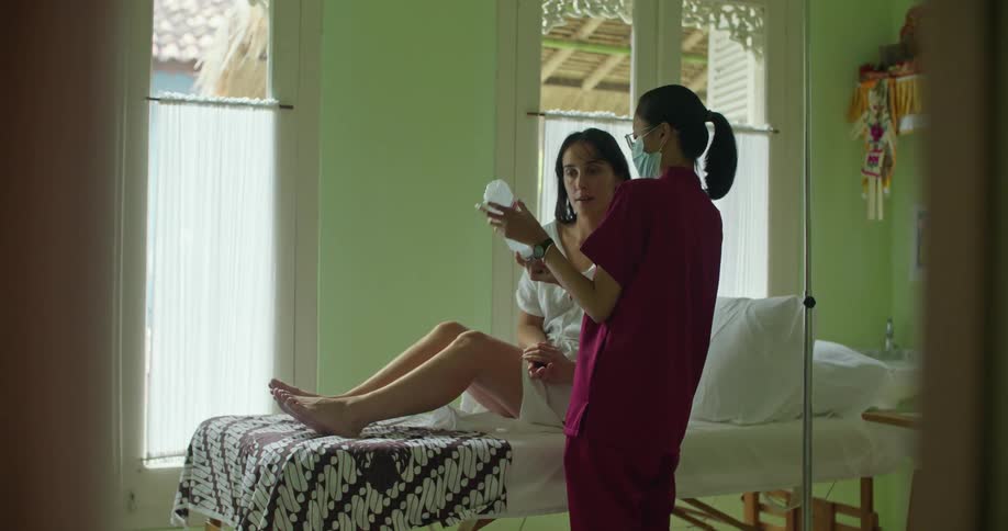 A woman is sitting up in bed as she speaks to a nurse who is showing her a bottle and giving her instructions